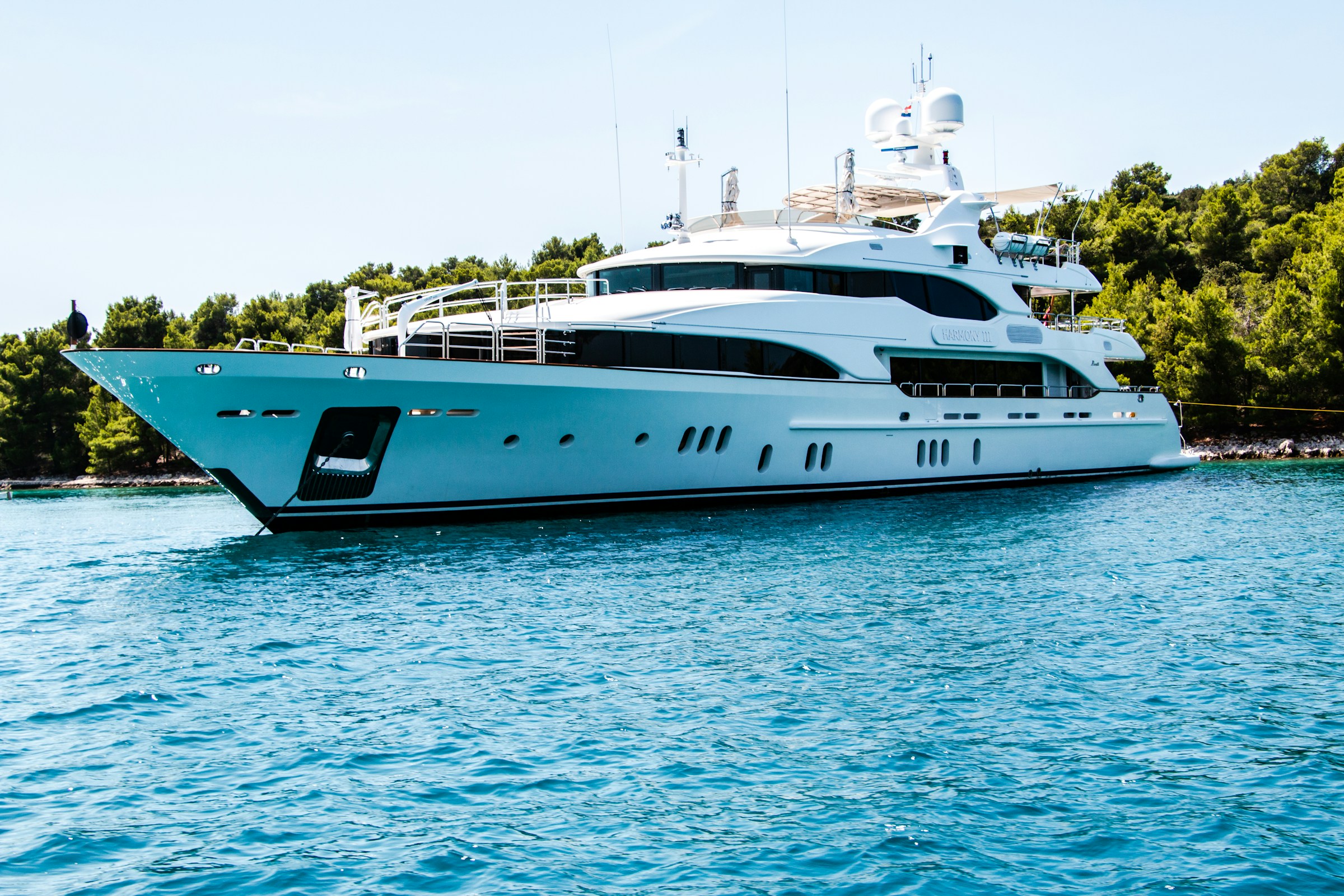 A white motor yacht anchored beside a wooded coastline